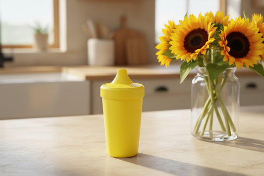 Yellow no splill sippy cup on a kitchen benchtop with sunflowers
