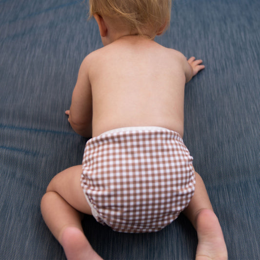 Happy toddler wearing a Tyoub fawn check reusable swim nappy on a carpet.