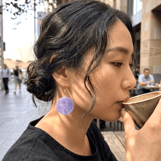 On-model style photo showcasing the drop length, transparency, and geometric scale of the upcycled clear purple round dangle earrings.