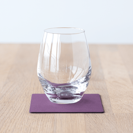 Square recycled leather coaster featuring the signature LIND DNA hippo texture on a table with a glass.