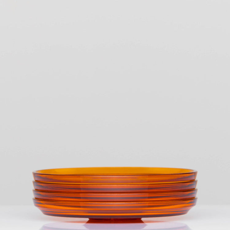 Pack of 4 HuskeeRenew translucent reusable small 3oz espresso saucers featuring the signature vertical ribbed design made from high-performance recycled polymer side view in amber.