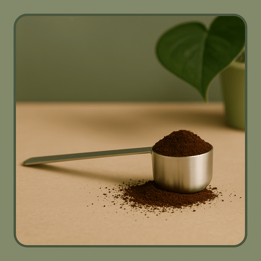 Long-handled stainless steel coffee measuring scoop spoon for filling reusable pods on a countertop with ground coffee.