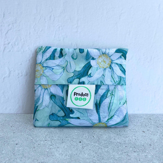 Close up view of the lightweight sixty gram reusable grocery bag folded entirely inside its own integrated self storing travel pouch for compact pocket storage. Flannel flower variant.