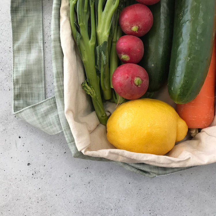 Single Produce Pod reusable veggie storage bag featuring a custom Gum leaf print standing open filled with fresh veg and fruit closeup with lemon on a stone background.