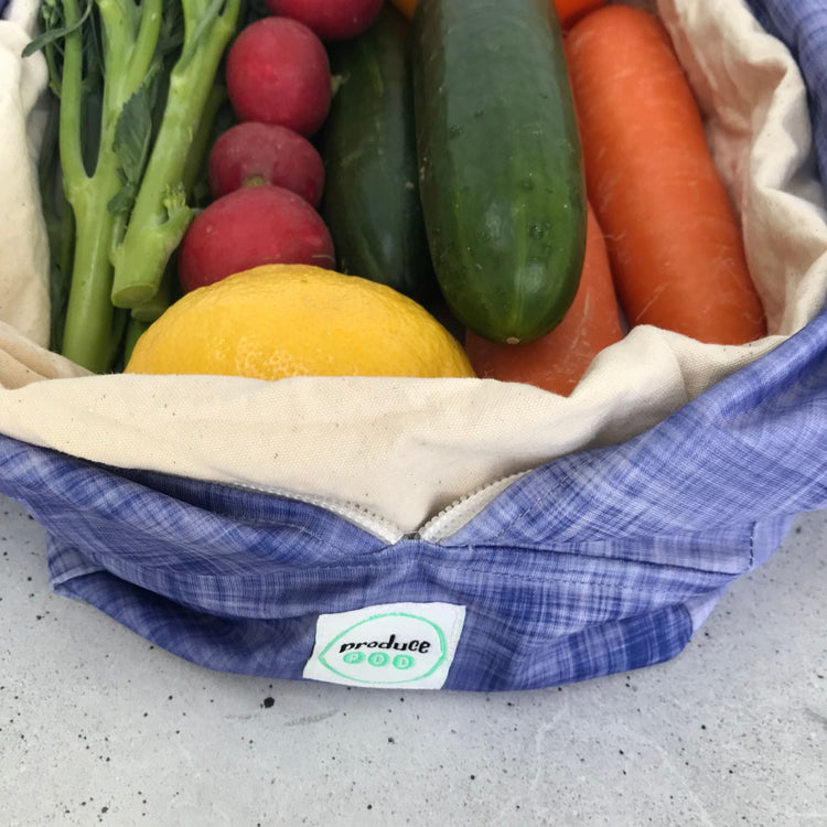 Single Produce Pod reusable veggie storage bag featuring a custom Plum print standing open filled with fresh veg and fruit closeup with zucchin, carrot, radish and broccolini.
