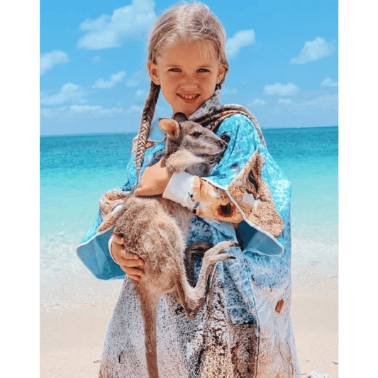 Young girl on a sandy beach wearing the Kalbarri print quick dry kids hooded towel.