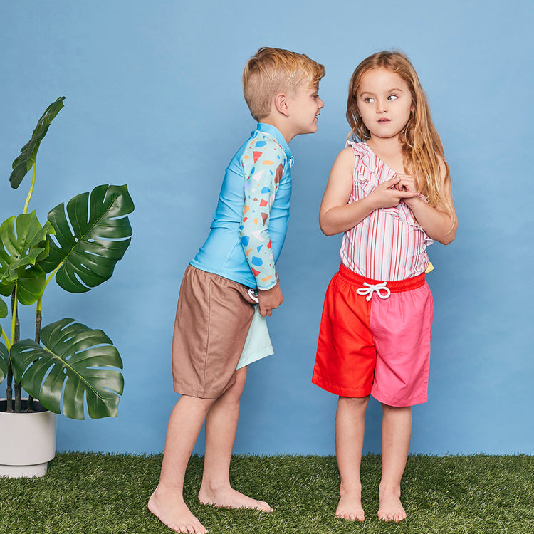 Young boy wearing a Tyoub long sleeve turquoise ocean glass rashie and matching board shorts in a studio setting side view.