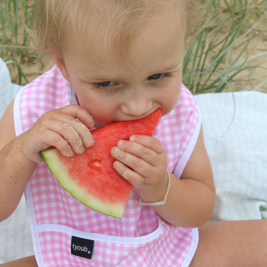 Happy toddler using a waterproof baby bib in pink check with an integrated crumb catch-all front pocket.