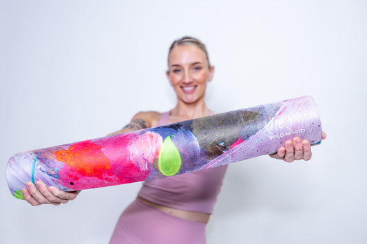 Woman holding a Flamingle Yoga Mat by Wild Mingo in a Yoga studio against a white wall