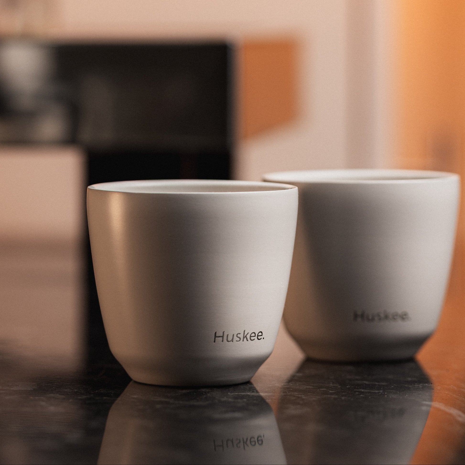 Set of 2 HuskeeSteel 3oz espresso cups crafted from 91% recycled double-wall vacuum insulated stainless steel on a counter in a cafe.