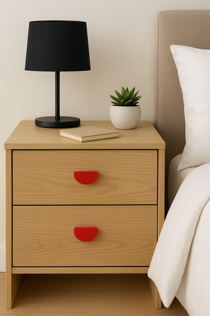 Wooden nightstand with red recycled plastic  handles, black lamp, and a plant in a small white pot next to a bed.