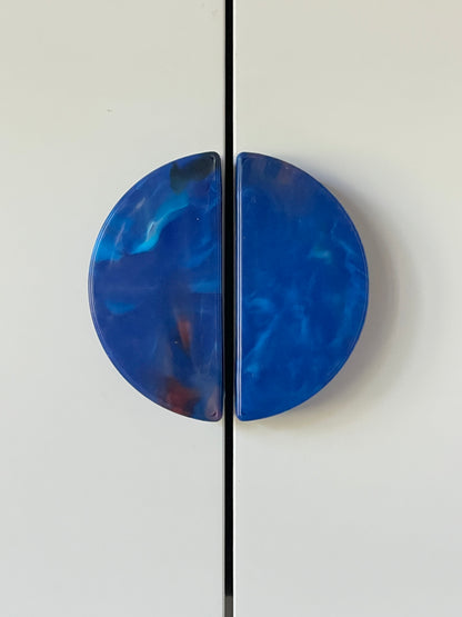 Two blue, semi-circular cabinet handles made from recycled plastic on a white cupboard.
