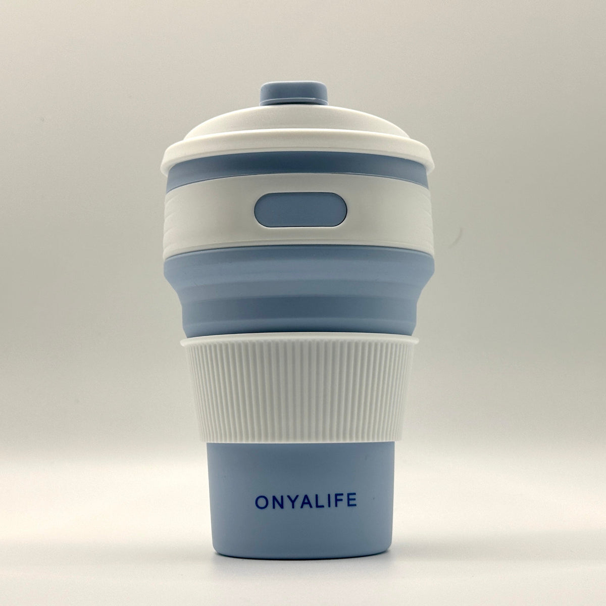 Collapsible 350ml silicone coffee cup with secure lid and heat-protective sleeve, shown expanded and collapsed with its reusable storage pouch. Shown in Powder Blue