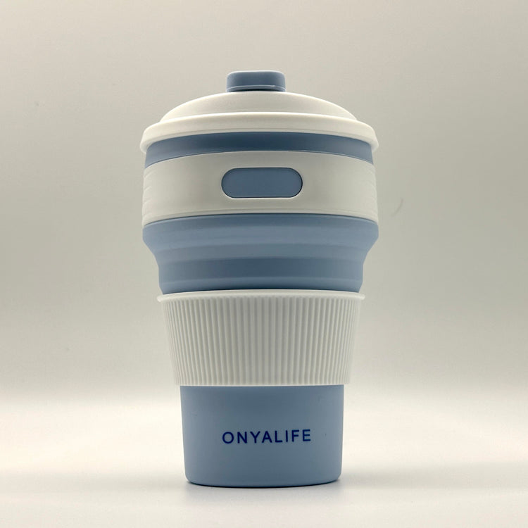 Collapsible 350ml silicone coffee cup with secure lid and heat-protective sleeve, shown expanded and collapsed with its reusable storage pouch. Shown in Powder Blue