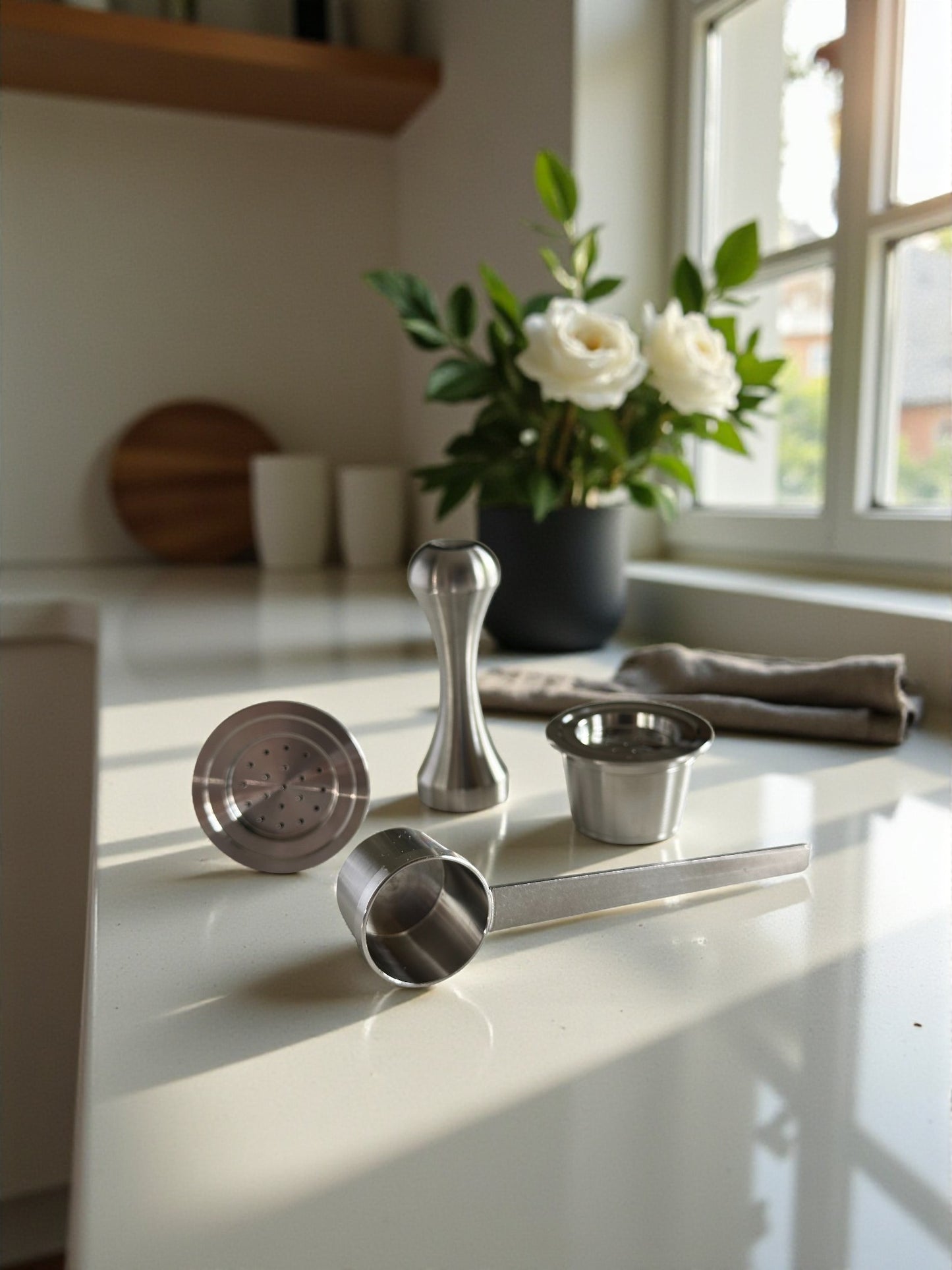 Two Pod Star Espressotoria stainless steel reusable coffee pods on a kitchen bench with a tamper and scoop