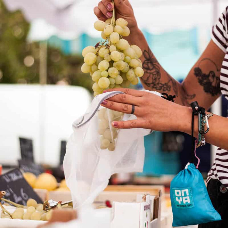 A person putting grapes into an ONYA reusable mesh produce bag, 100% rPET, see through mesh with draw string closure.