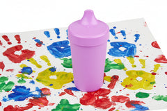 Purple no spill sippy cup sitting on a child's finger painting