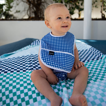 Happy toddler wearing a Tyoub blue check waterproof bib near an outdoor pool in Australia.