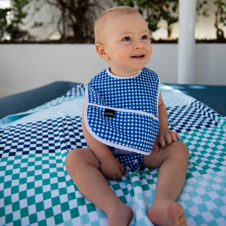 Happy toddler wearing a Tyoub blue check waterproof bib near an outdoor pool in Australia.