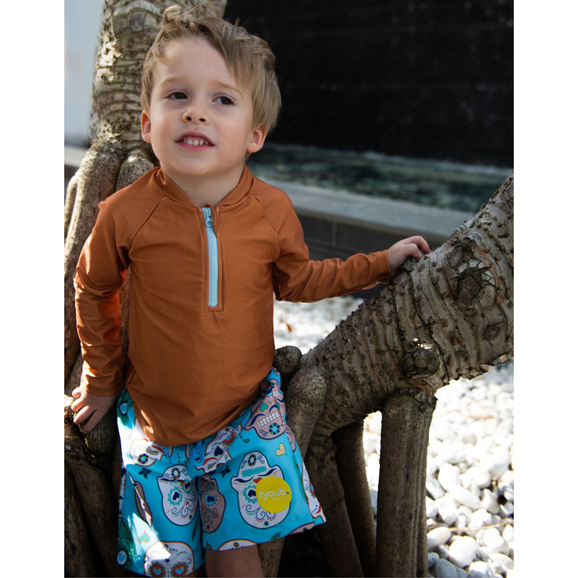 Young boy wearing aqua sugar skull pattern swim boardshorts outdoors in Australia.
