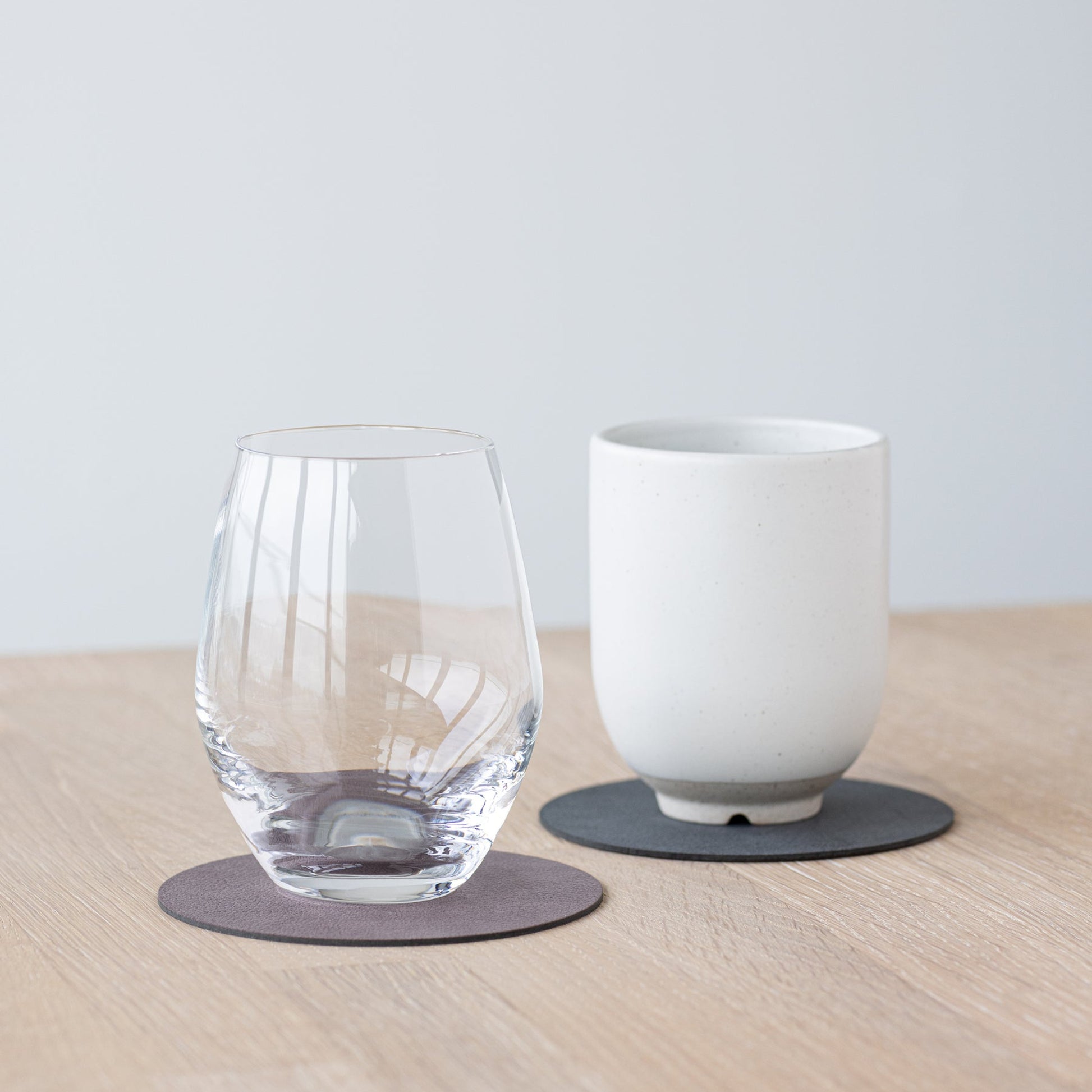 Two circle recycled leather coasters showing two different colours and textures with a glass and a cup.