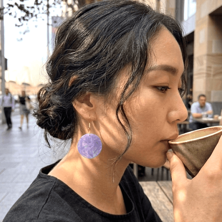 On-model style photo showcasing the drop length, transparency, and geometric scale of the upcycled clear purple round dangle earrings.
