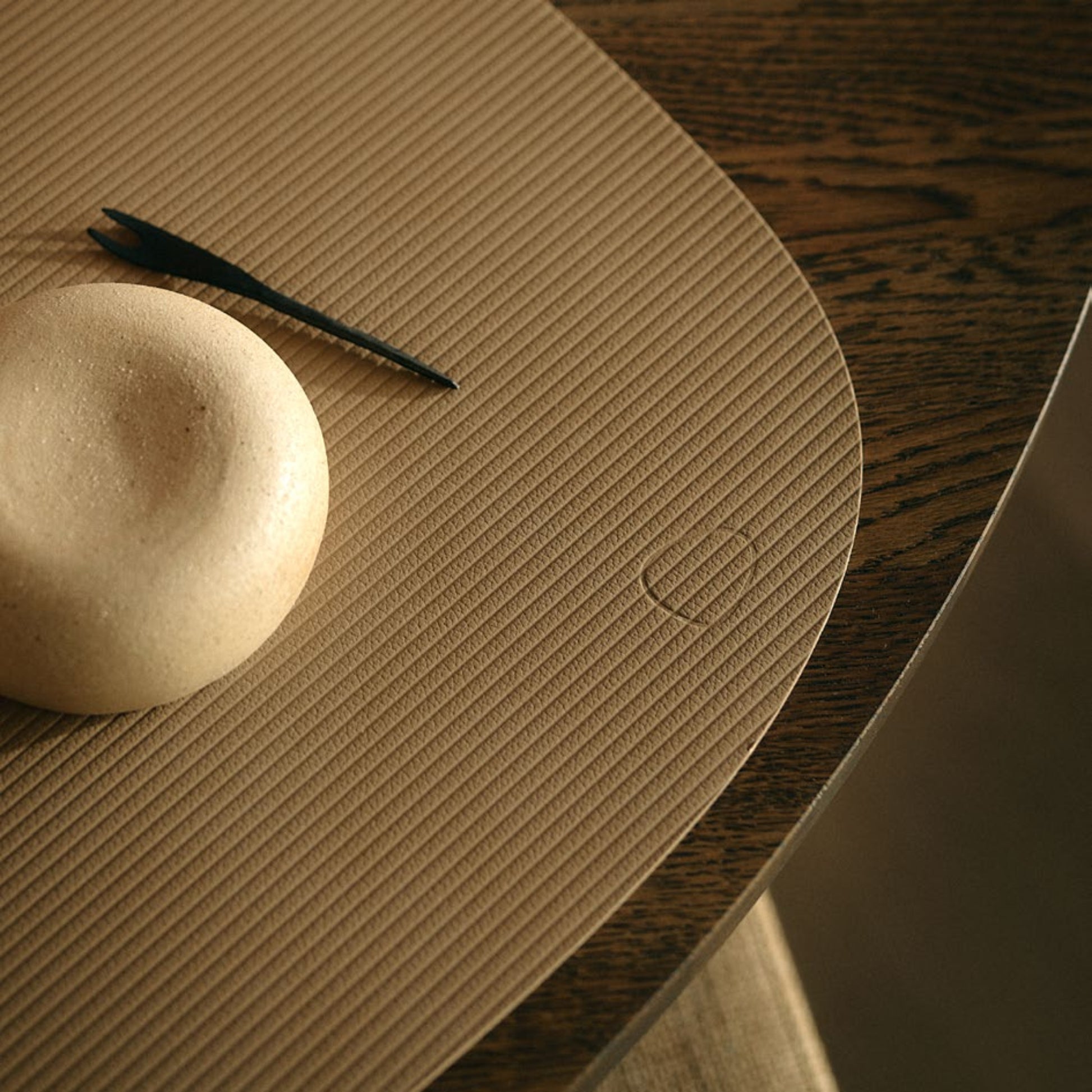 Curve recycled leather placemat featuring the signature LIND DNA corduroy texture close up on a table with a smooth stone and pen.