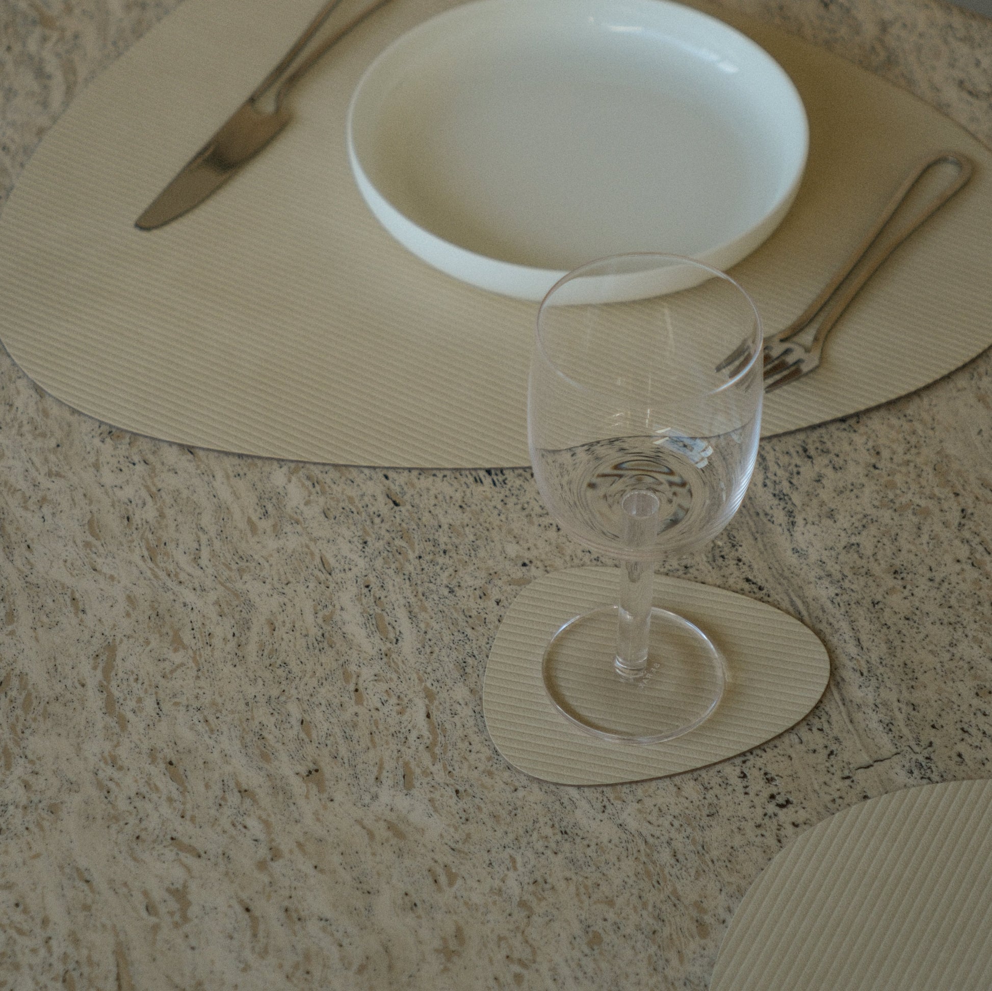 Curve recycled leather placemat featuring the signature LIND DNA corduroy texture on a marble table showing placemat, coaster,plate, cutlry and glassware.
