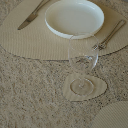 Curve recycled leather placemat featuring the signature LIND DNA corduroy texture on a marble table showing placemat, coaster,plate, cutlry and glassware.