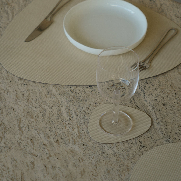 Curve recycled leather placemat featuring the signature LIND DNA corduroy texture on a marble table showing placemat, coaster,plate, cutlry and glassware.