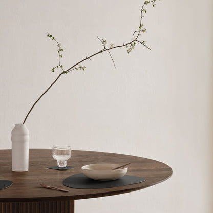 Wooden table with Curve recycled leather placemat featuring the signature LIND DNA Core texture with vase, bowl, fork and glass on a neutral background