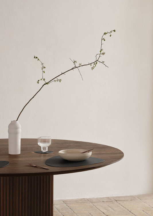 Wooden table with recycled leather table mat,  vase, bowl, and glass on a neutral background