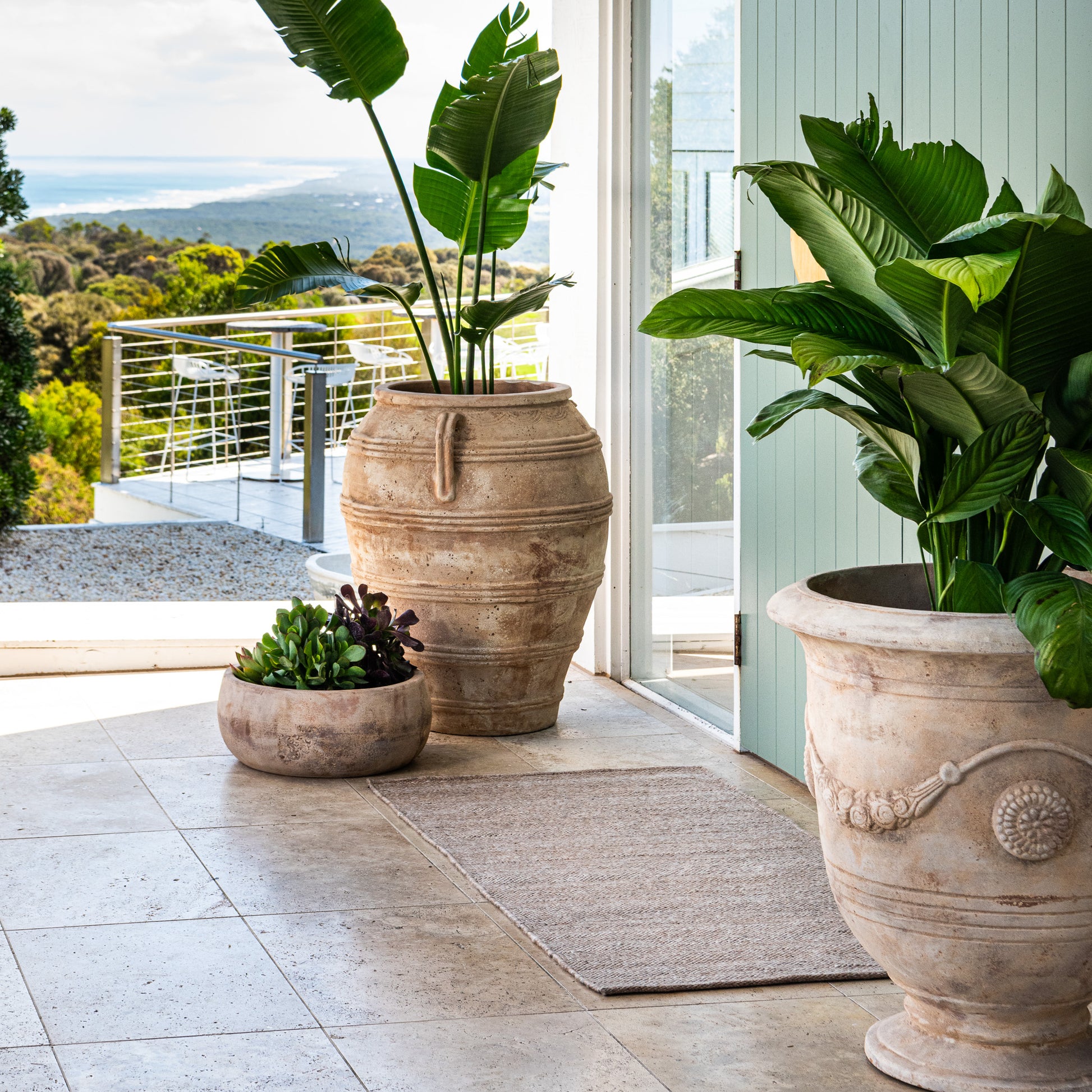 Durable Zebra Home Fraser beige flatweave runner rug styled next to large potted plants on a balcony patio.