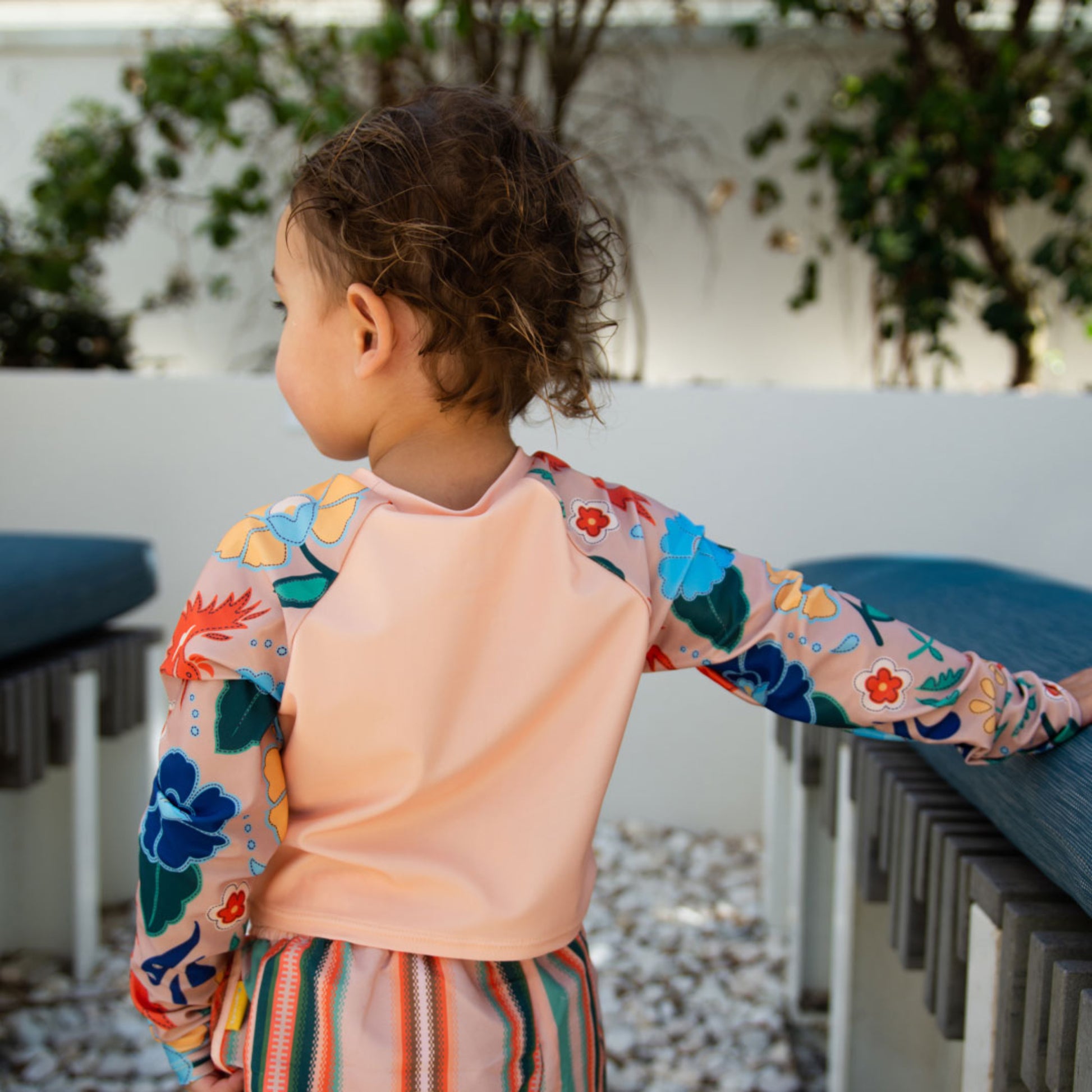 Young girl wearing the Tyoub long sleeve vanilla phoenix rash vest by a pool back view with matching shorts..