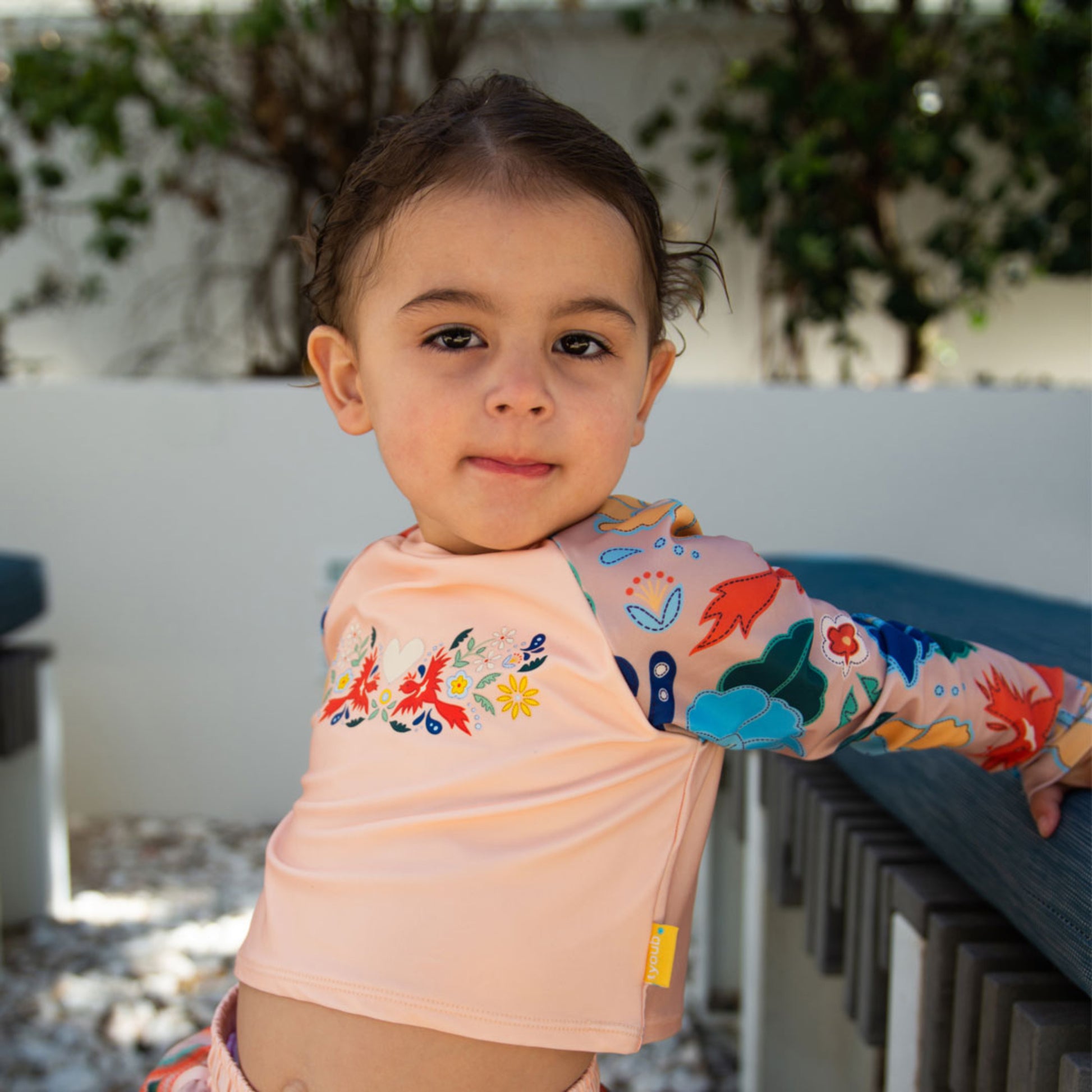 Young girl wearing the Tyoub long sleeve vanilla phoenix rash vest by a pool for UV sun protection in Australia.