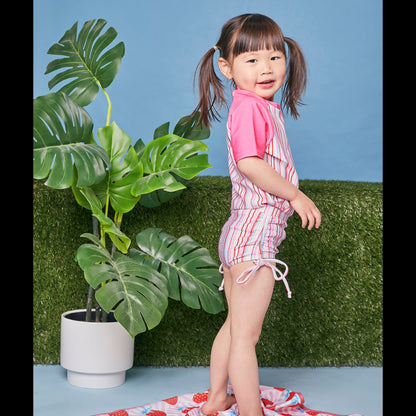 Young girl modeling the Tyoub short sleeve gelato pink striped rash vest with matching swimsuit side view.