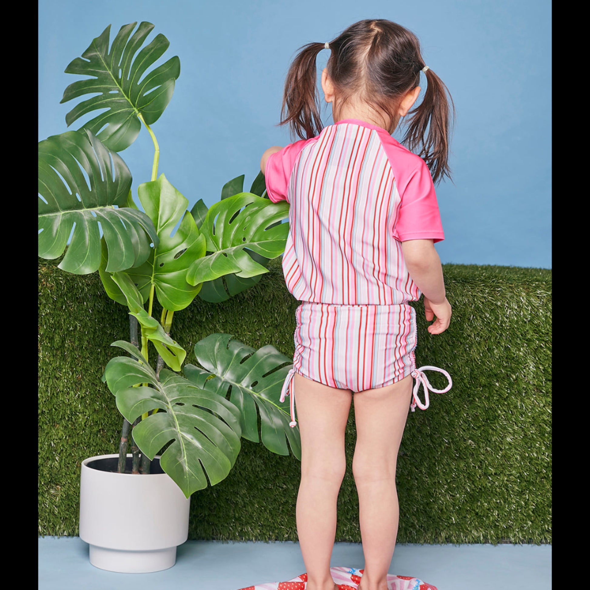 Girl modelling the Tyoub short sleeve gelato pink striped rash vest with matching swimsuit back view.