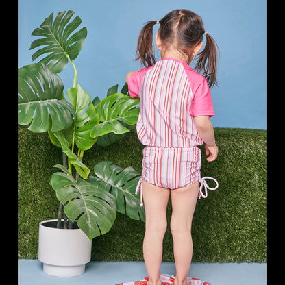 Girl modelling the Tyoub short sleeve gelato pink striped rash vest with matching swimsuit back view.