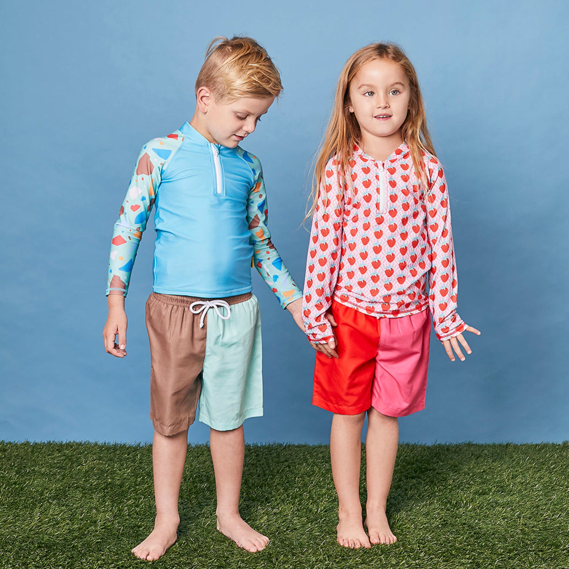 Young girl wearing the Tyoub strawberry sundae rash guard paired with pink swim board shorts in a studio setting.