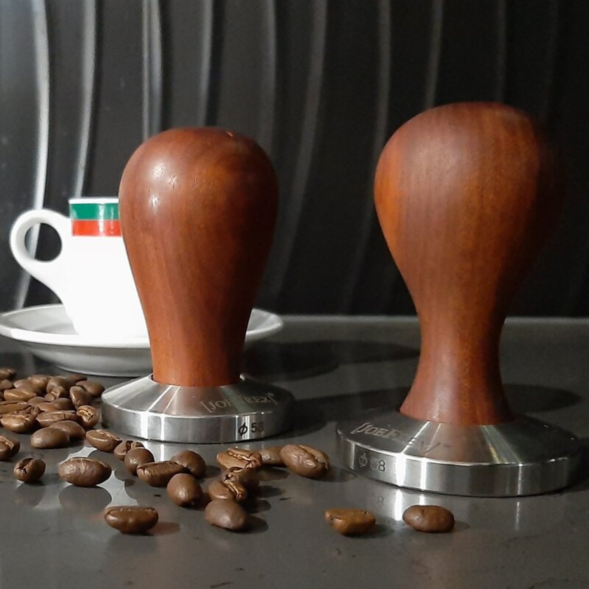 Two premium hand-turned recycled timber coffee tampers with a precision-weighted stainless steel base, handcrafted in Australia by Lyons Woodturning in use in a cafe with coffee beans and a cup of coffee.