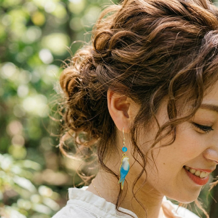 On-model style photo showcasing the fit, drop length, and scale of the colorful upcycled plastic bird silhouette earrings. Light blue and white vaiant.