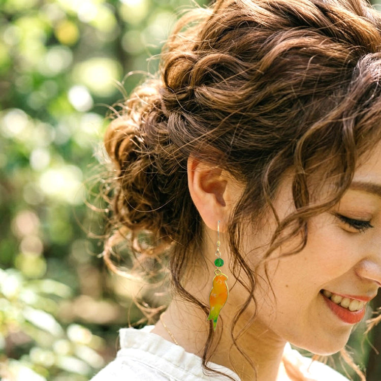 On-model style photo showcasing the fit, drop length, and scale of the colorful upcycled plastic bird silhouette earrings. Orange and light green variant.