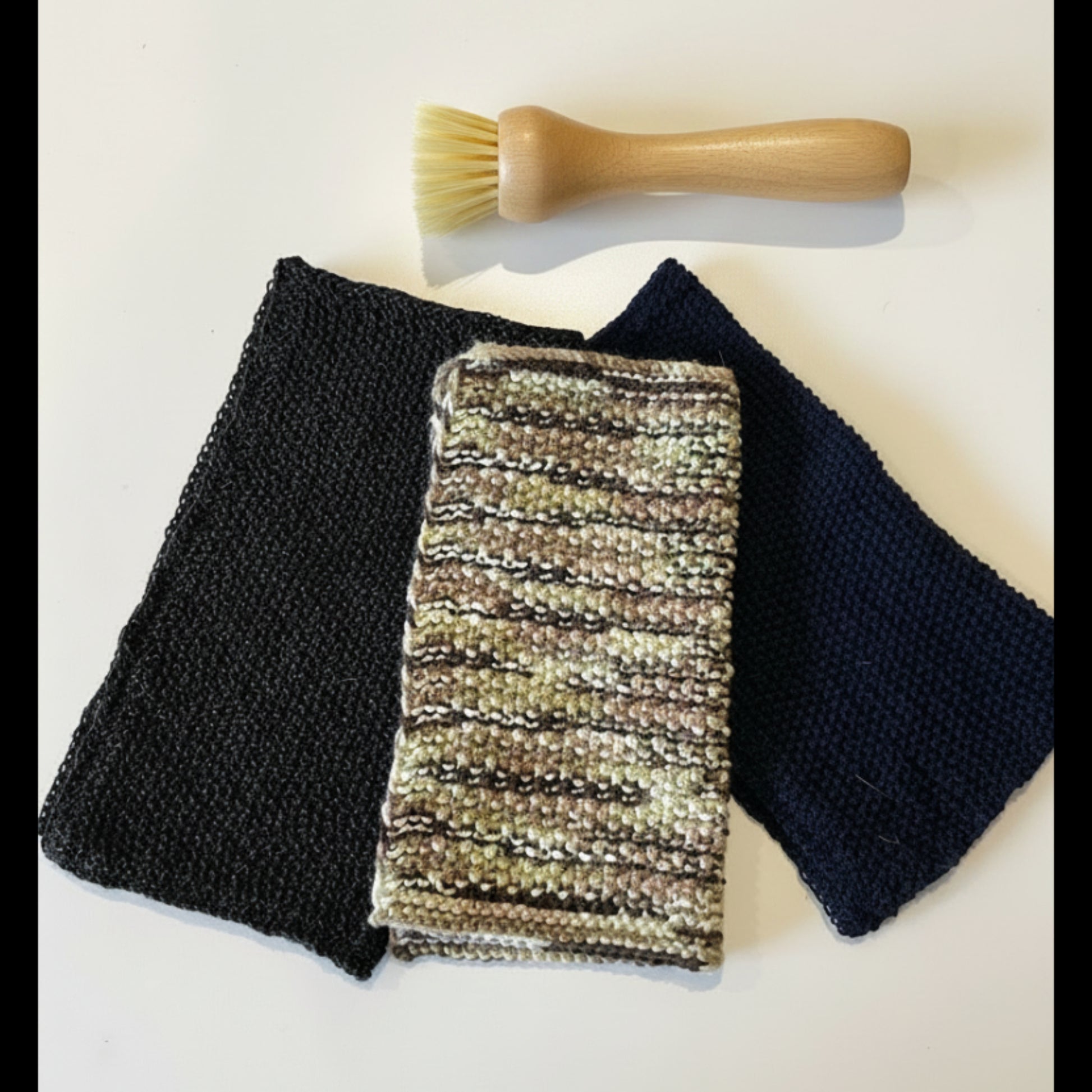 A textured upcycled acrylic dish scrubber cloth styled next to a small scrubbing brush, serving as an anti-odour, quick-drying alternative to synthetic kitchen sponges.
