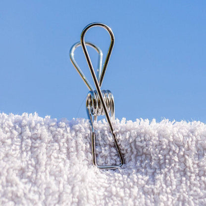 Close-up profile view of a single wire-formed rust-resistant stainless steel clothes peg displaying its ergonomic loop spring mechanics on a on a towel.