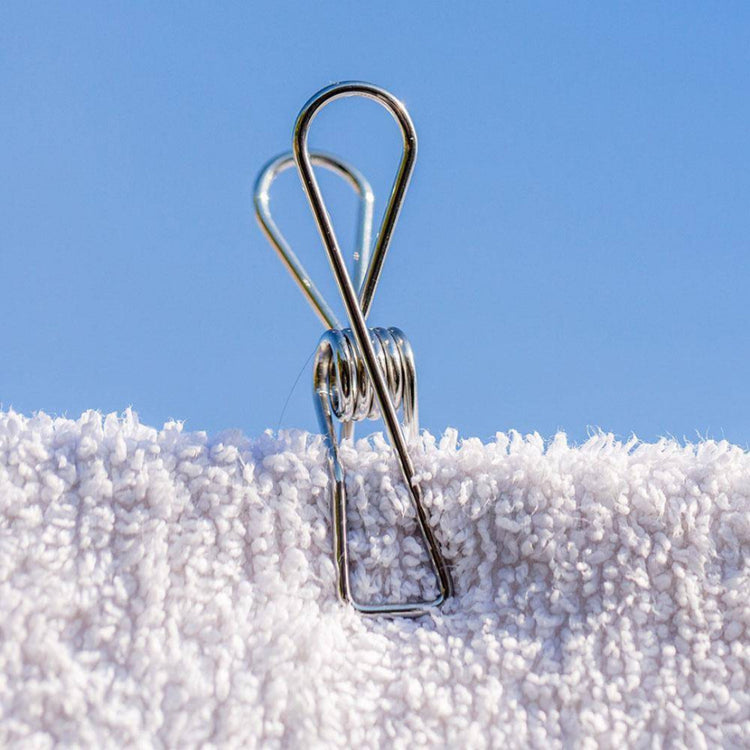 Close-up profile view of a single wire-formed rust-resistant stainless steel clothes peg displaying its ergonomic loop spring mechanics on a on a towel.