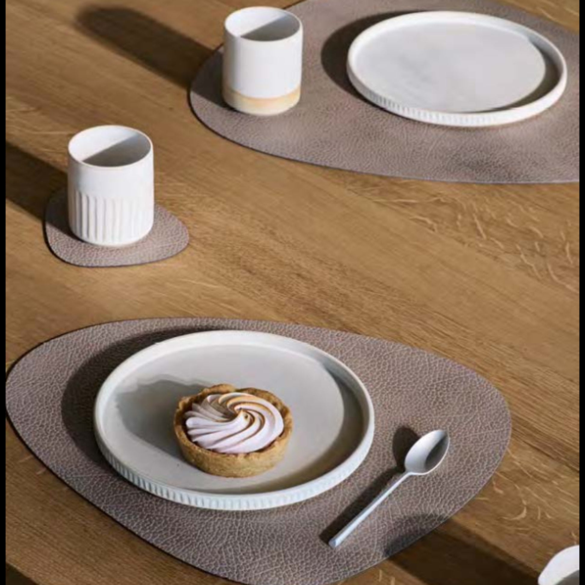 Curve recycled leather placemat featuring the signature LIND DNA Hipppo texture on a table set with plates, cups, tart and a spoon.