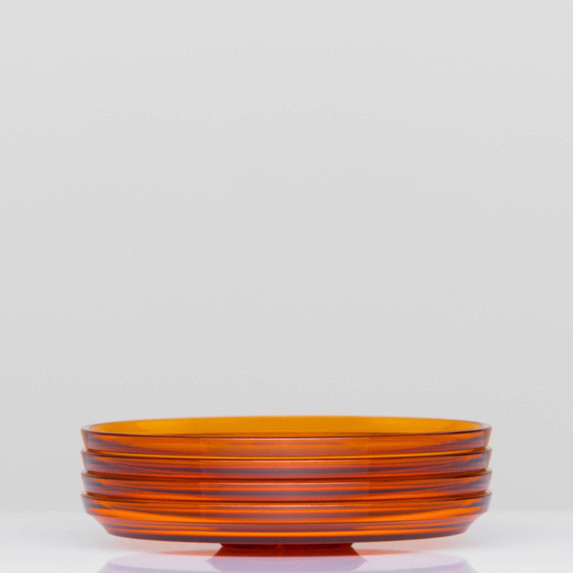 Pack of 4 HuskeeRenew translucent reusable small 3oz espresso saucers featuring the signature vertical ribbed design made from high-performance recycled polymer side view in amber.