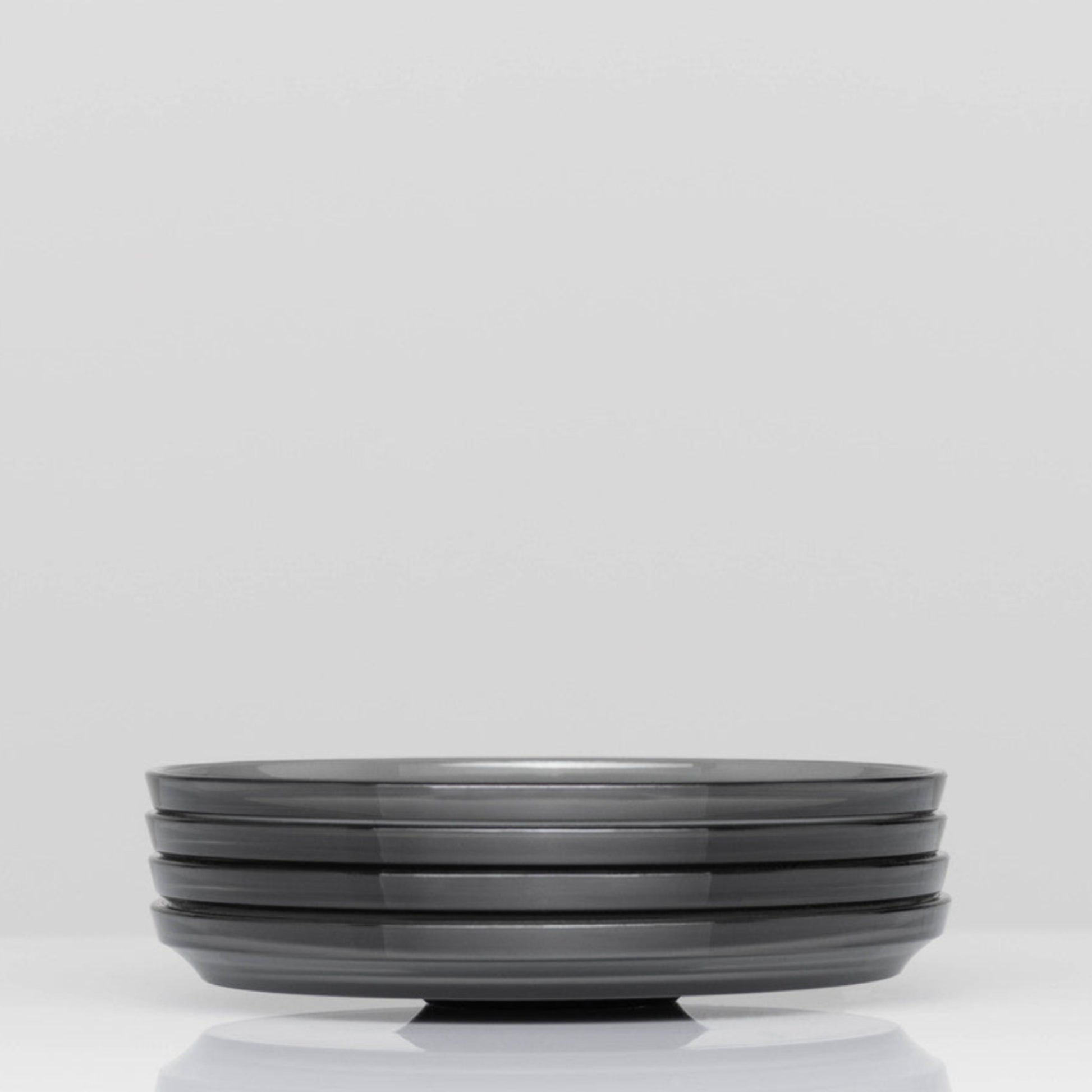 Pack of 4 HuskeeRenew translucent reusable small 3oz espresso saucers featuring the signature vertical ribbed design made from high-performance recycled polymer side view in smoke.