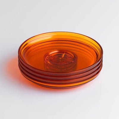 Pack of 4 HuskeeRenew translucent reusable small 3oz espresso saucers featuring the signature vertical ribbed design made from high-performance recycled polymer top view in amber.
