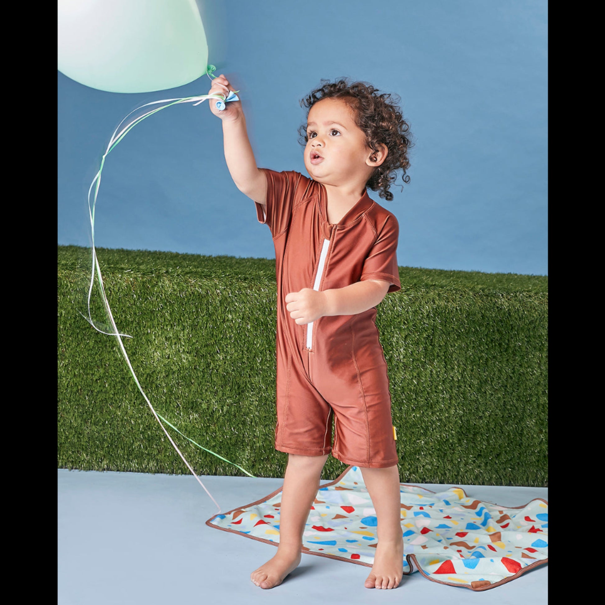 Young child playing in a studio wearing the Tyoub bear on the beach shorty sunsuit bather for UV protection.